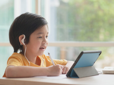 Kid with headphones learning from tablet while sitting on desk