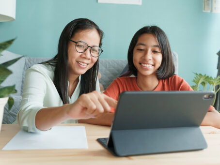 A girl and her mother smiling at laptop