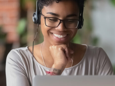Young woman with glasses and headphones smiling toward laptop