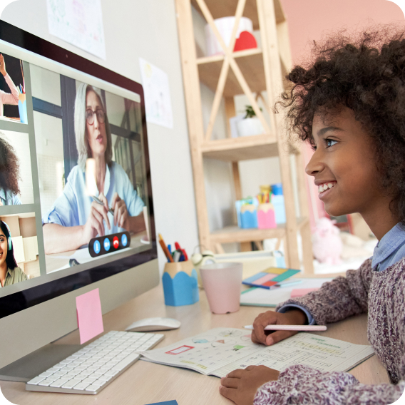 A young girl smiling at a monitor on a videocall with her teacher