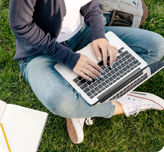 Girl's hands on a laptop keyboard, she is sitting on green grass